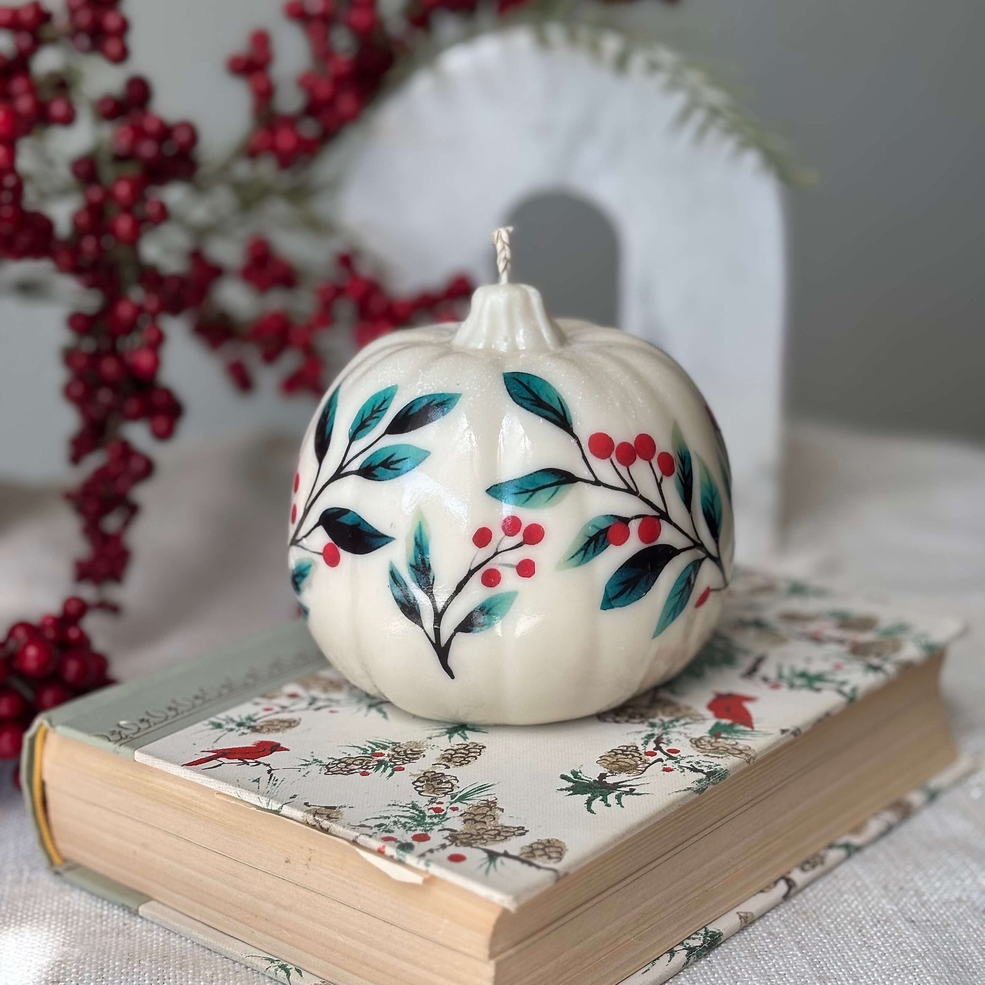 Decorative pumpkin-shaped candle with floral and berry design, placed on a festive holiday book — perfect handmade gift for Thanksgiving, Christmas, Halloween or fall birthday

