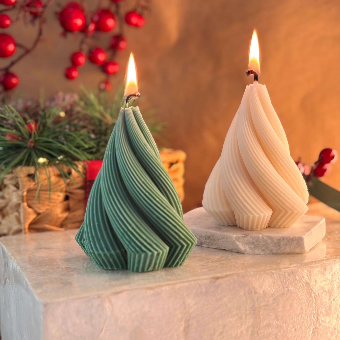 Green sculpted soy wax candle in the shape of a Christmas tree with elegant twisted design, next to an ivory version on a festive stone block

