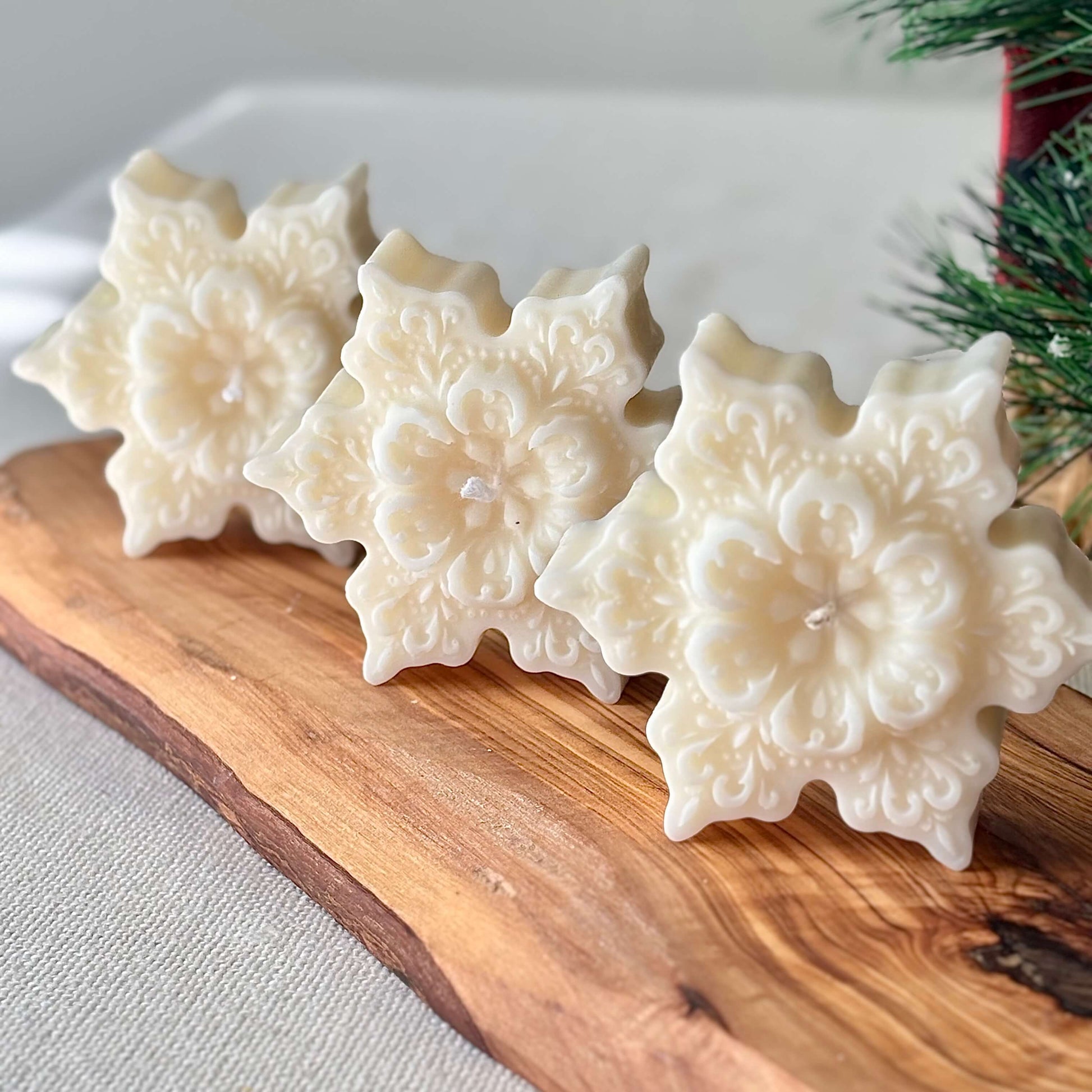 Three handmade snowflake soy candles with floral pattern on a wooden board