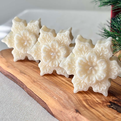 Three handmade snowflake soy candles with floral pattern on a wooden board