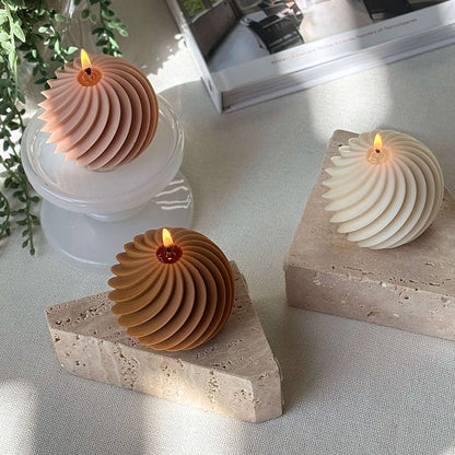 Three burning spiral sphere candles in peach, ivory and honey colors on marble and stone bases, cozy home gift decor.