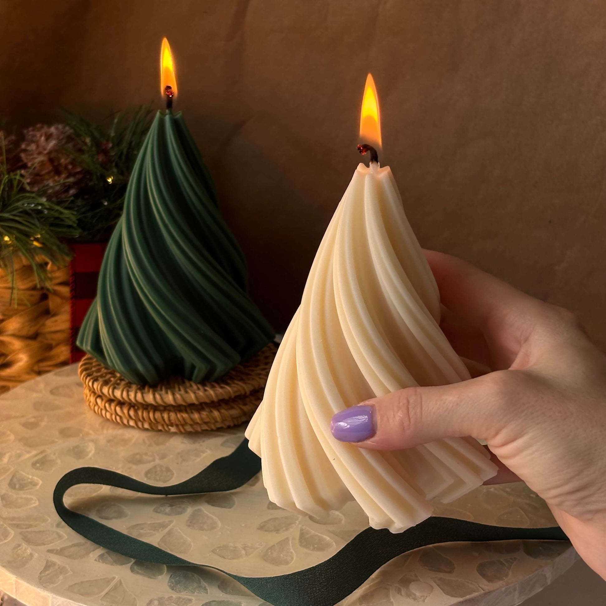 Woman holding beige tree-shaped candle with purple nails, green tree candle glowing in background — perfect Christmas gift for mom or friend.