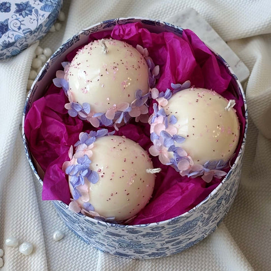 Top view of Bloomella luxury round flower candles, set of three, nestled in a gift box with fuchsia tissue.	
