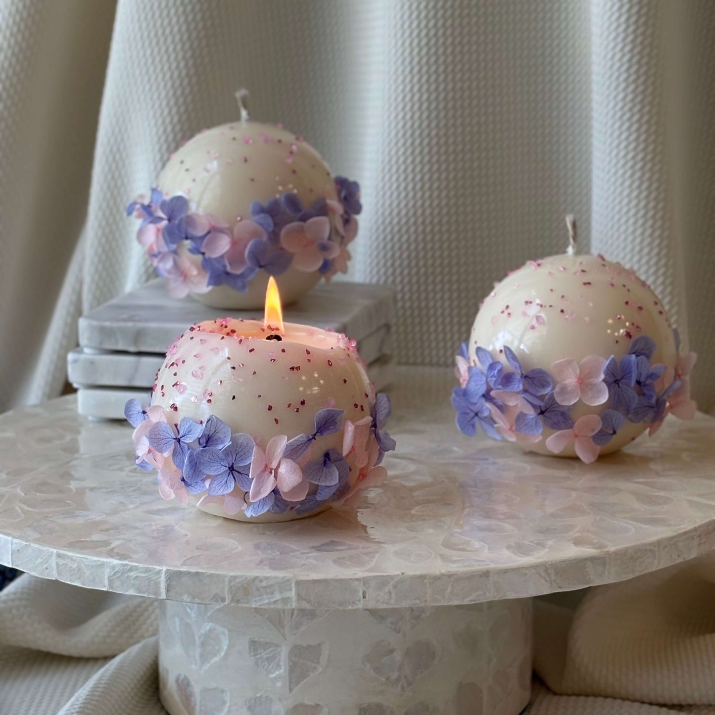 Trio of Bloomella flower candles with center candle burning, showing even melt pool and petal detail.	