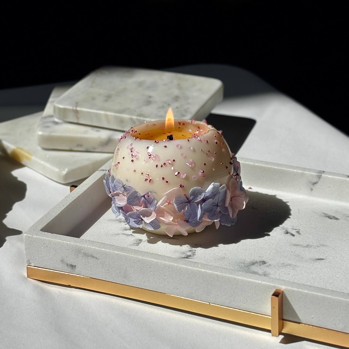 Hand-poured Bloomella flower candle lit in natural sunlight on a marble tray — clean burn showcase.	