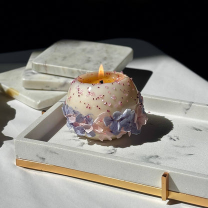Hand-poured Bloomella flower candle lit in natural sunlight on a marble tray — clean burn showcase.	