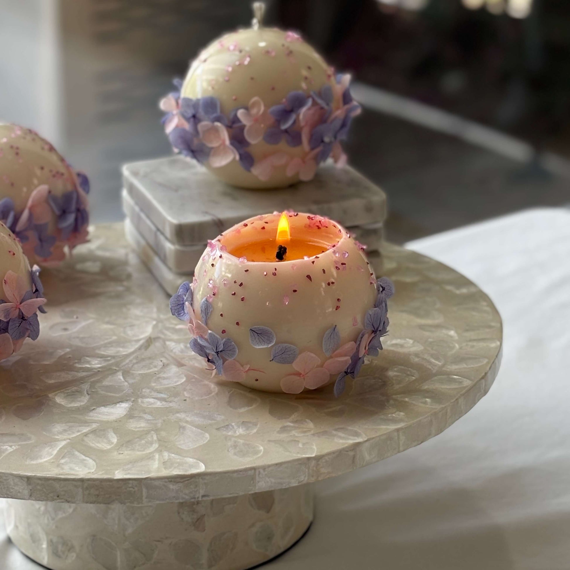Bloomella round flower candle burning on a marble pedestal — handmade soy wax coffee-table décor.	