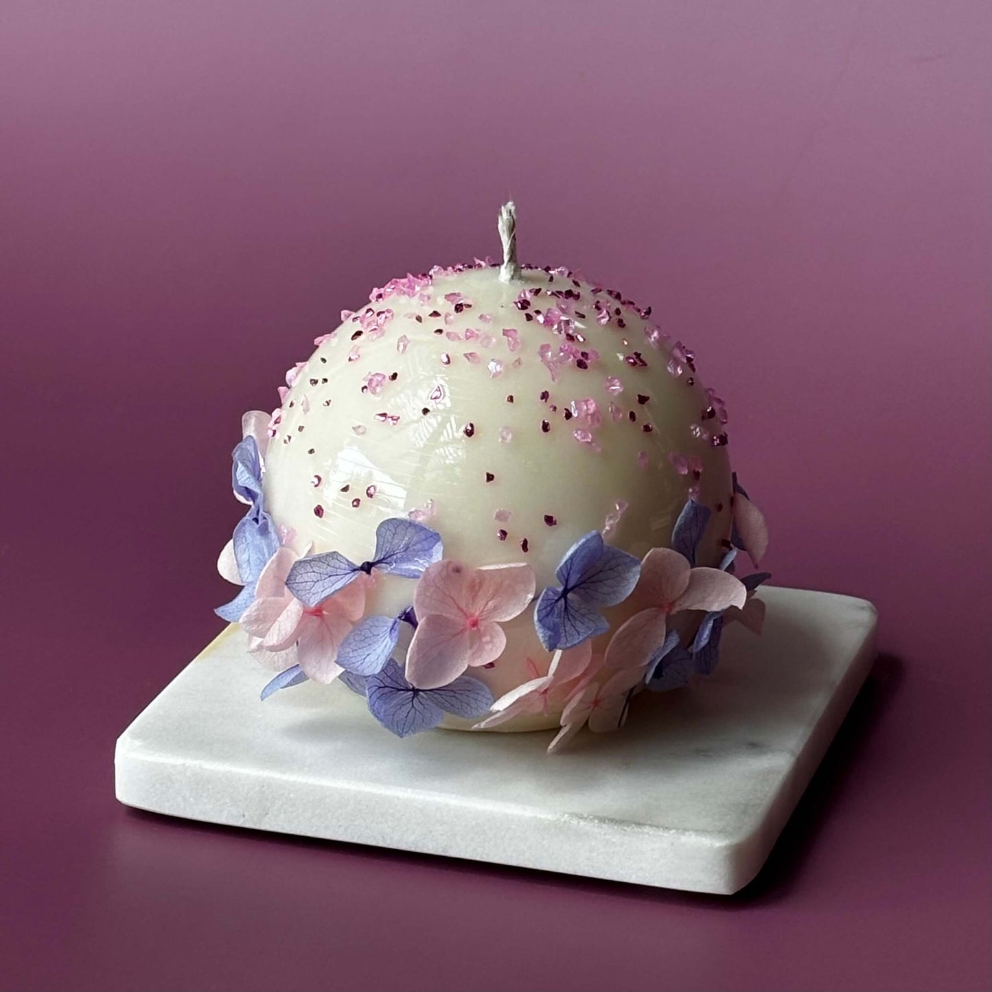 Single Bloomella handmade flower candle on lavender backdrop highlighting glossy finish and hydrangea petals.	