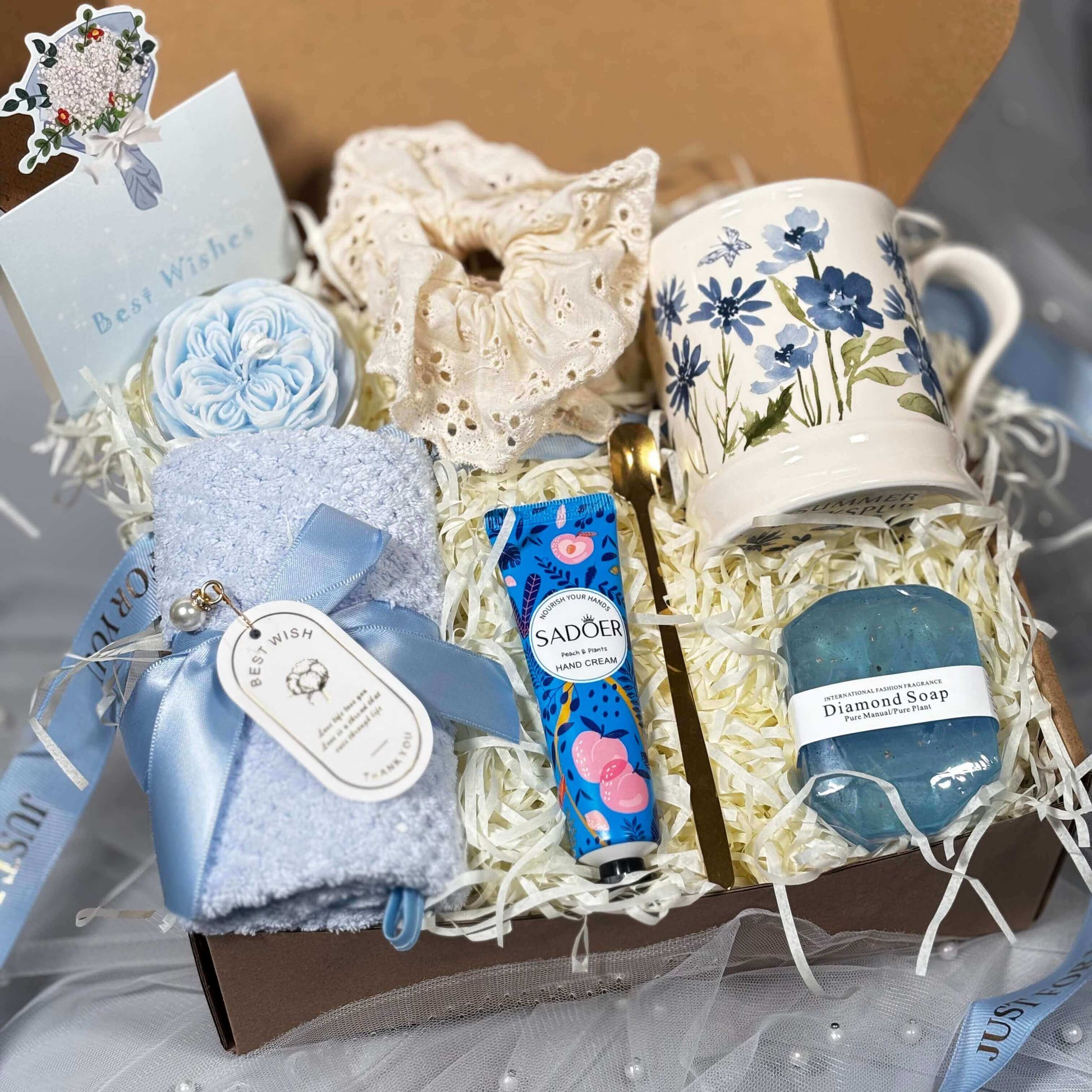 Top view of a blue-themed spa gift box for women with floral mug, blue diamond soap, rose candle, towel, hand cream, and scrunchie – a perfect self-care and birthday gift.
