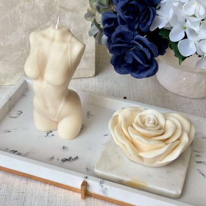Handmade sculptural torso candle and rose candle on marble tray with floral background