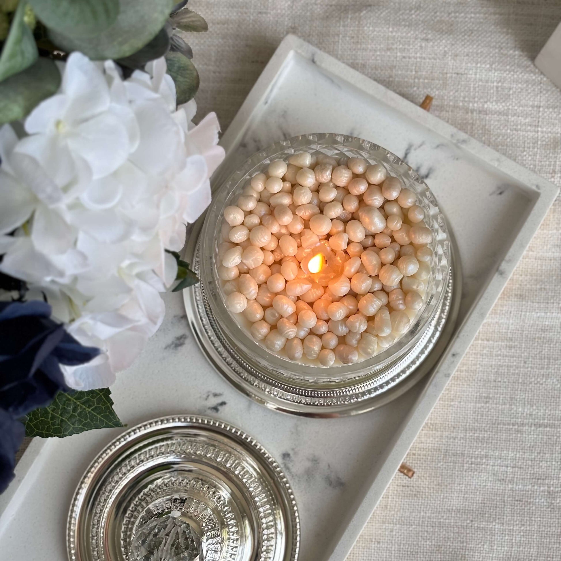 Burning pearl candle surrounded by flowers — luxury wedding gift and elegant décor for any interior


