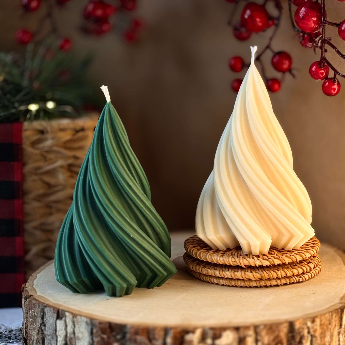 Two spiral handmade candles shaped like Christmas trees, one green and one ivory, displayed on rustic wood with festive berries in the background