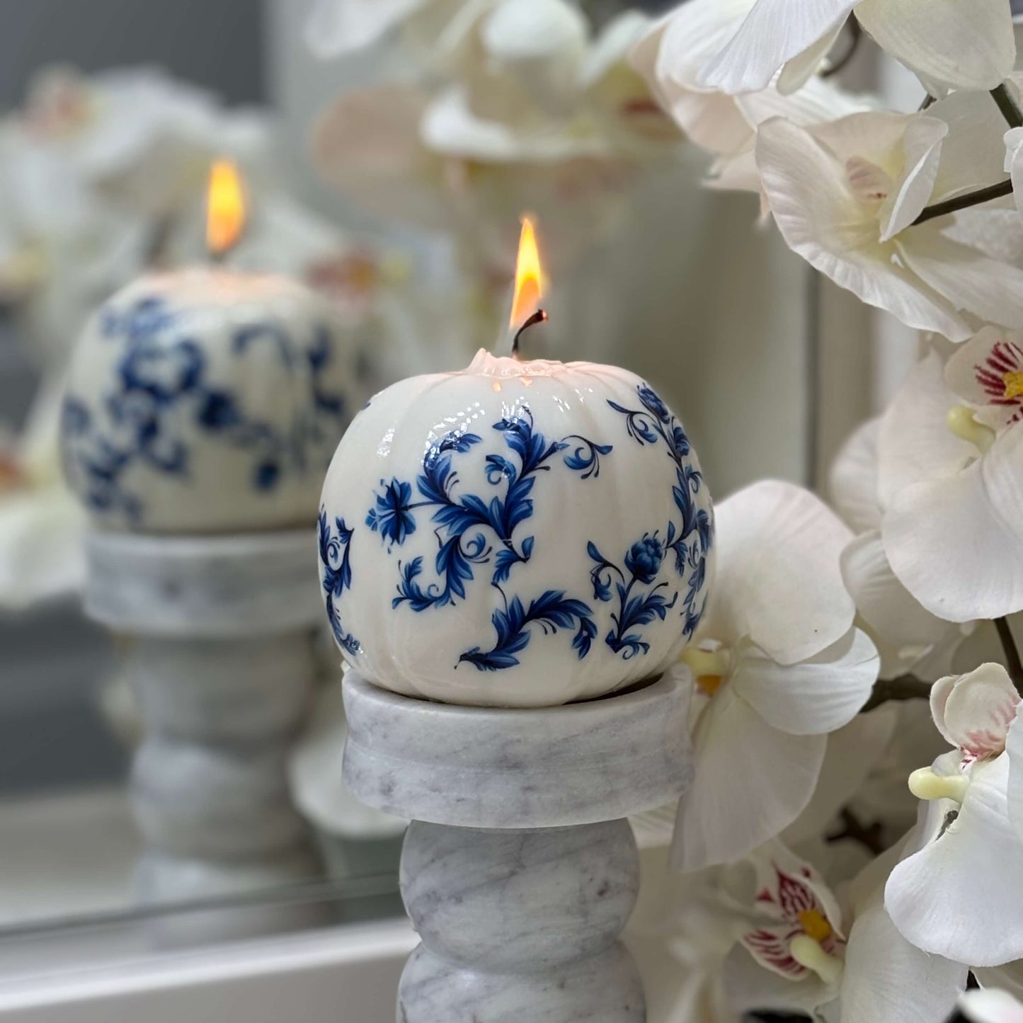 Decorative candle in Delft blue ceramic style, placed on a marble candleholder with white orchid flowers for luxury home decor.