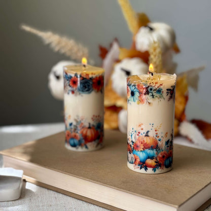 Two diamond glossy pumpkin candles with floral autumn design on wooden book surface