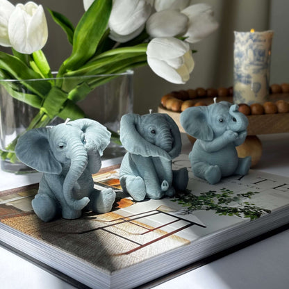 Multiple handmade soy wax elephant candles arranged in a round wicker basket, with tulips and decorative candles in the background.