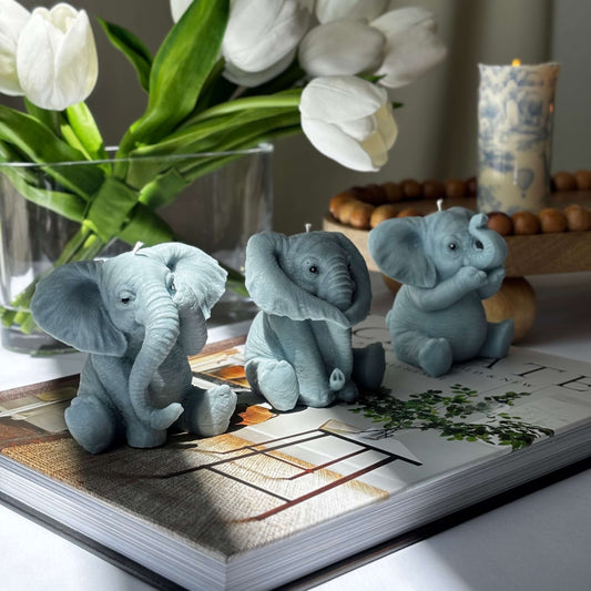 Multiple handmade soy wax elephant candles arranged in a round wicker basket, with tulips and decorative candles in the background.