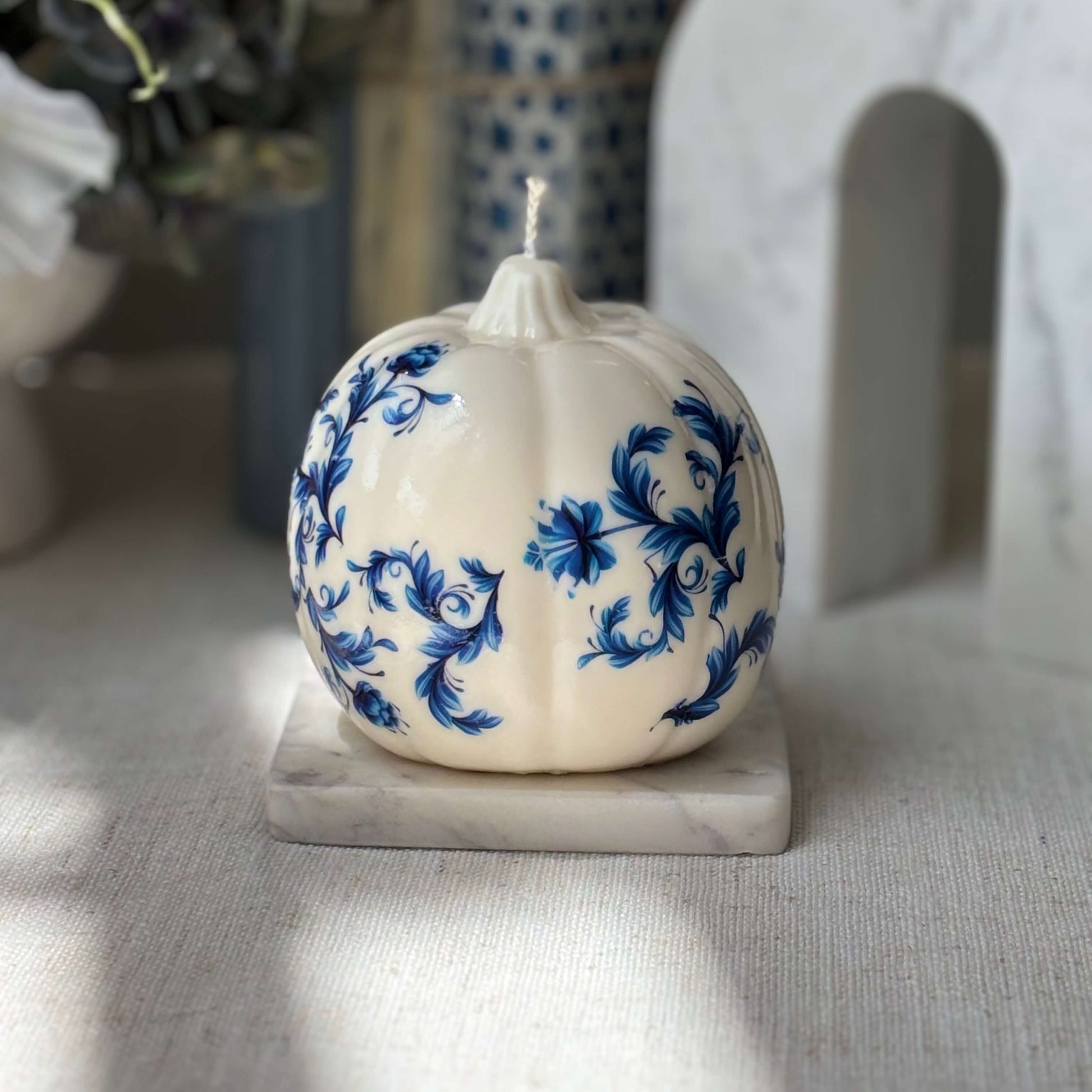 Large glossy pumpkin candle with blue and white floral pattern, placed on marble for elegant fall table styling and cozy interior decor.

