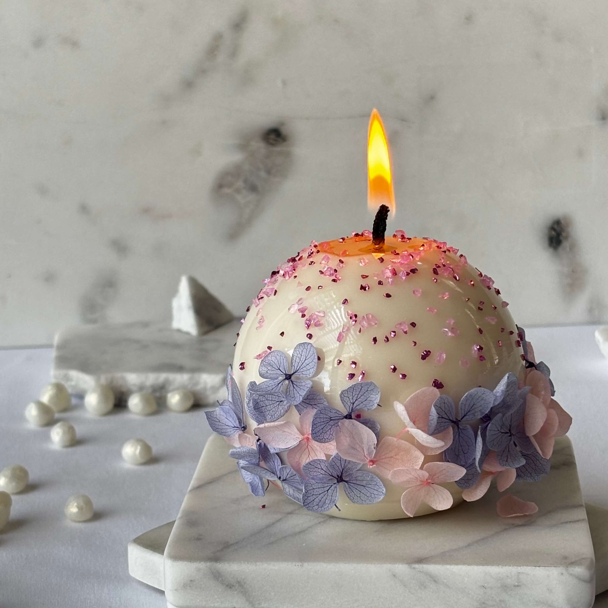 Burning round flower candle with pastel hydrangeas on marble tiles, romantic handmade decor