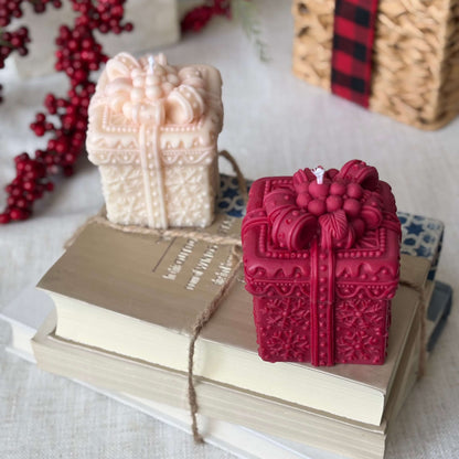 Red and beige gift box candles styled on stacked books with holiday berry decor.