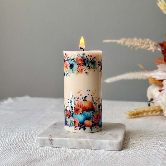 Glossy pumpkin candle with floral autumn design on marble coaster