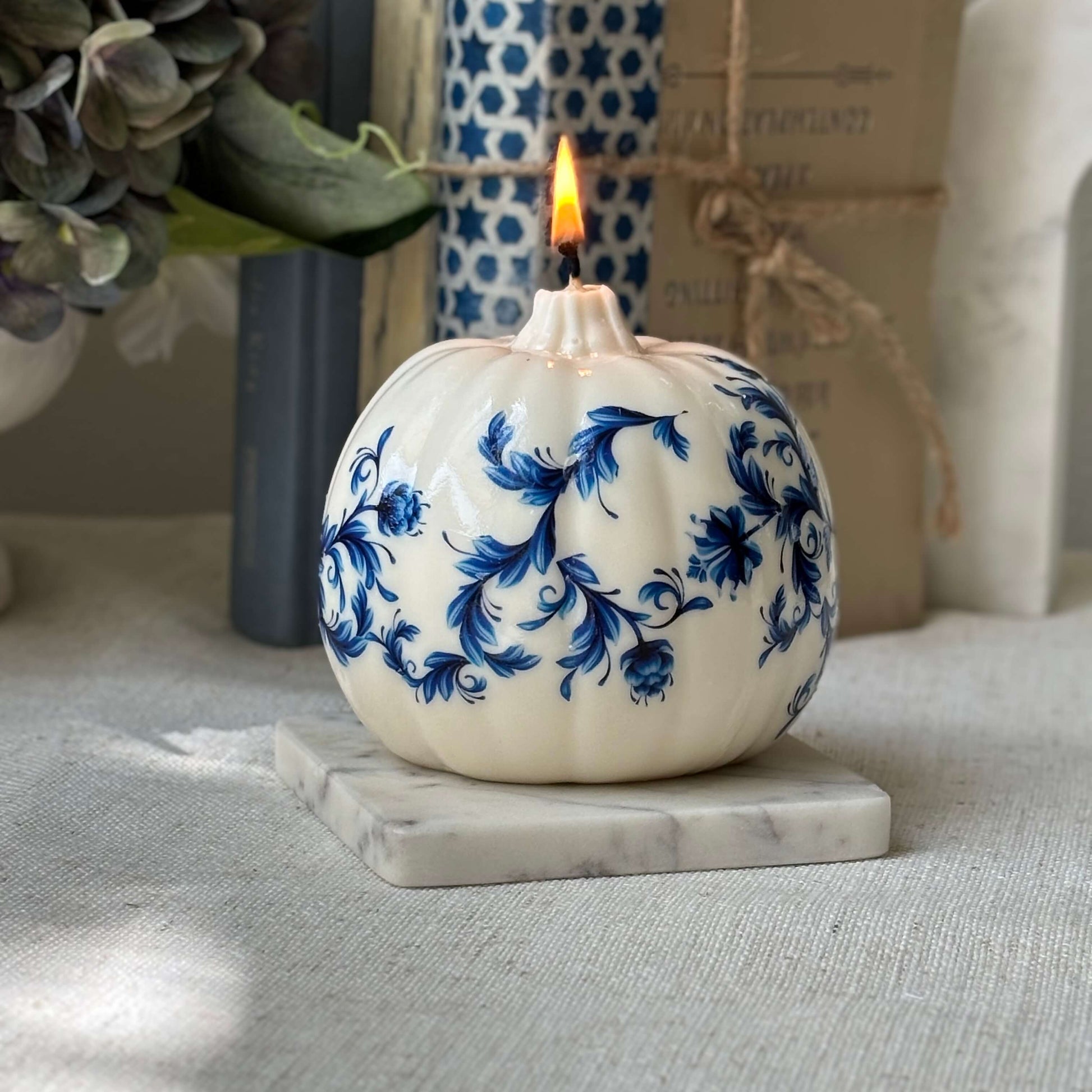 Glossy pumpkin-shaped candle with royal blue floral print, styled on a marble coaster for elegant white and blue decor.