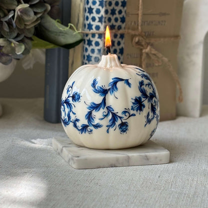 Glossy pumpkin-shaped candle with royal blue floral print, styled on a marble coaster for elegant white and blue decor.