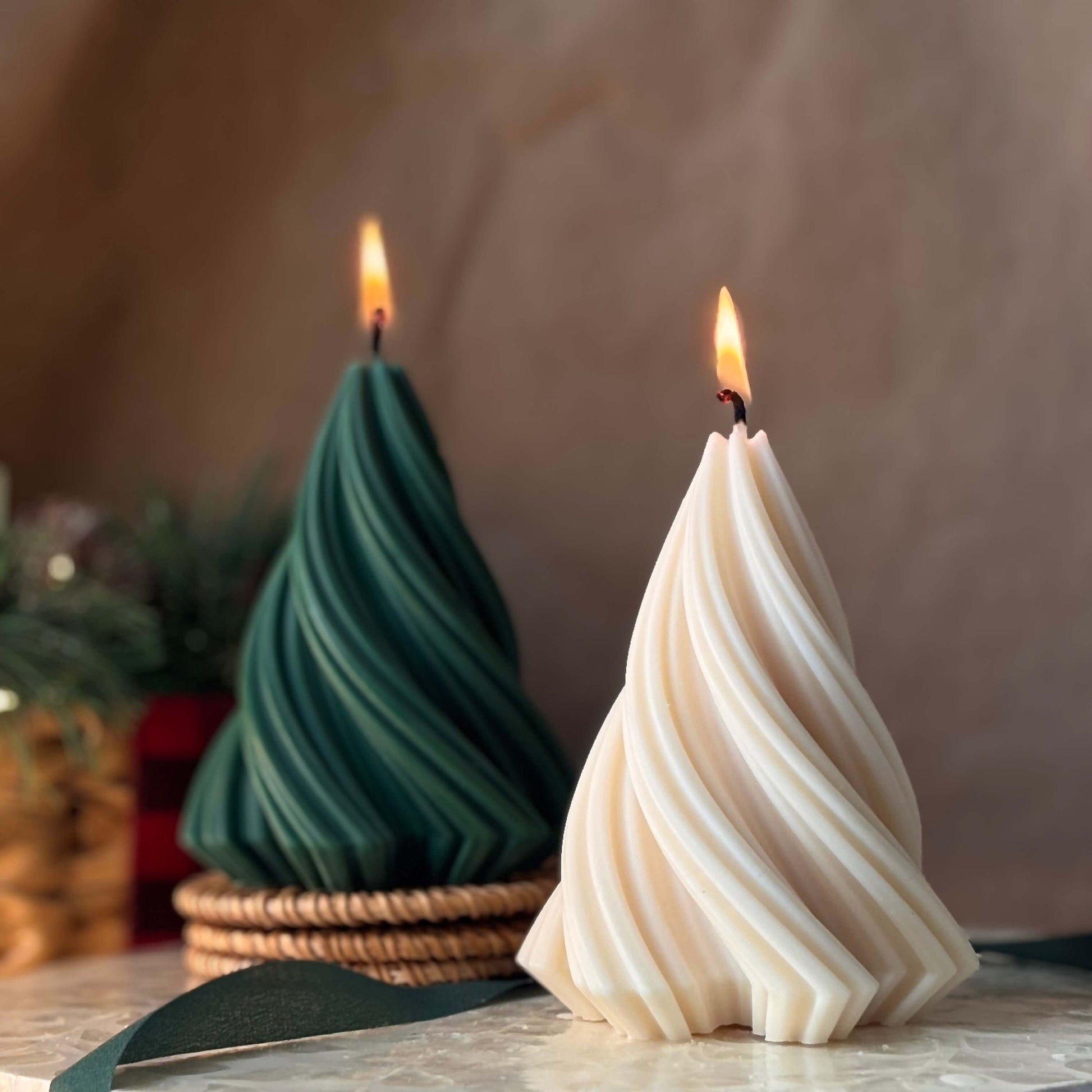 Lit soy wax Christmas candles in tree shape, green and beige, burning on a holiday table with festive background

