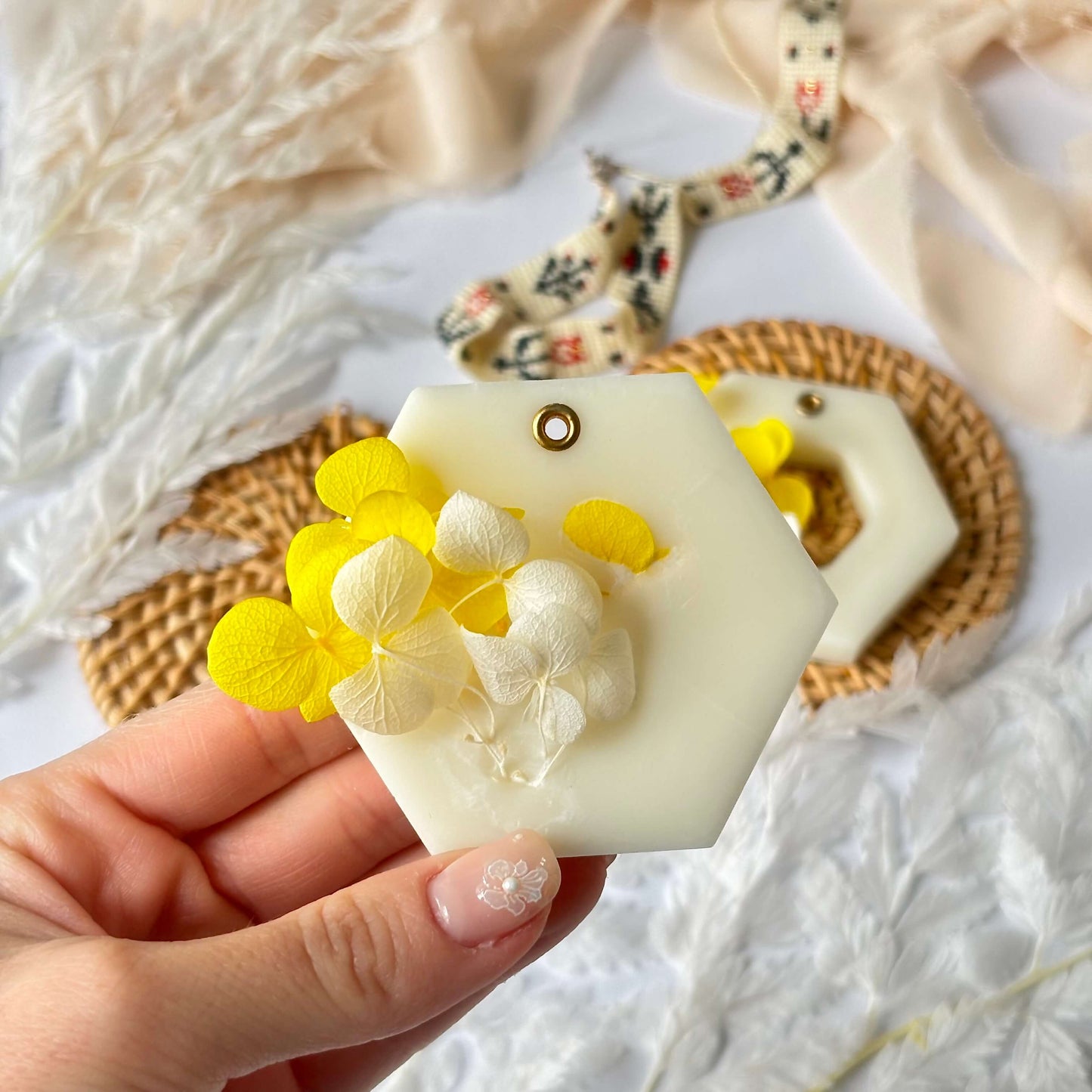 Hand holding a handmade soy wax aroma sachet with dried yellow and white flowers, against a cozy neutral background – botanical scent made in the USA.