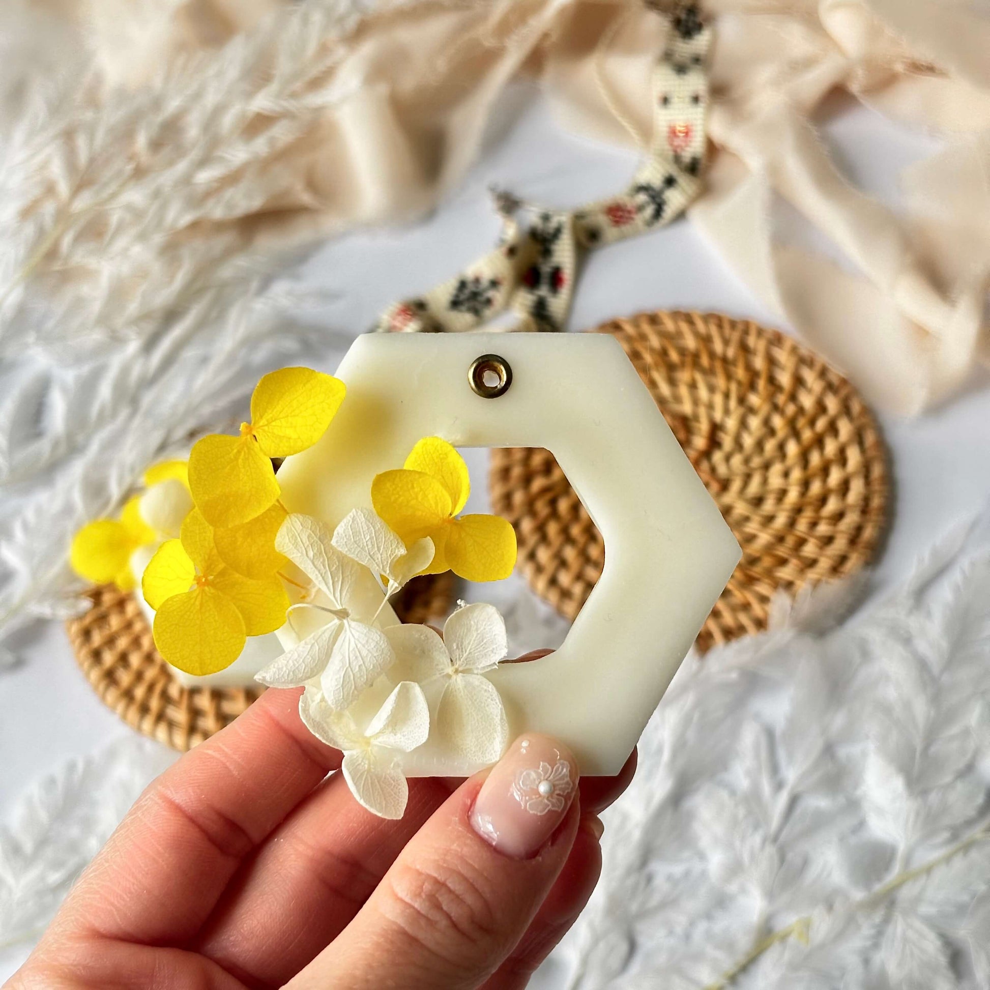 Close-up of a handmade hexagon soy wax sachet with yellow and white dried flowers, held in hand against a soft natural background – crafted in California.