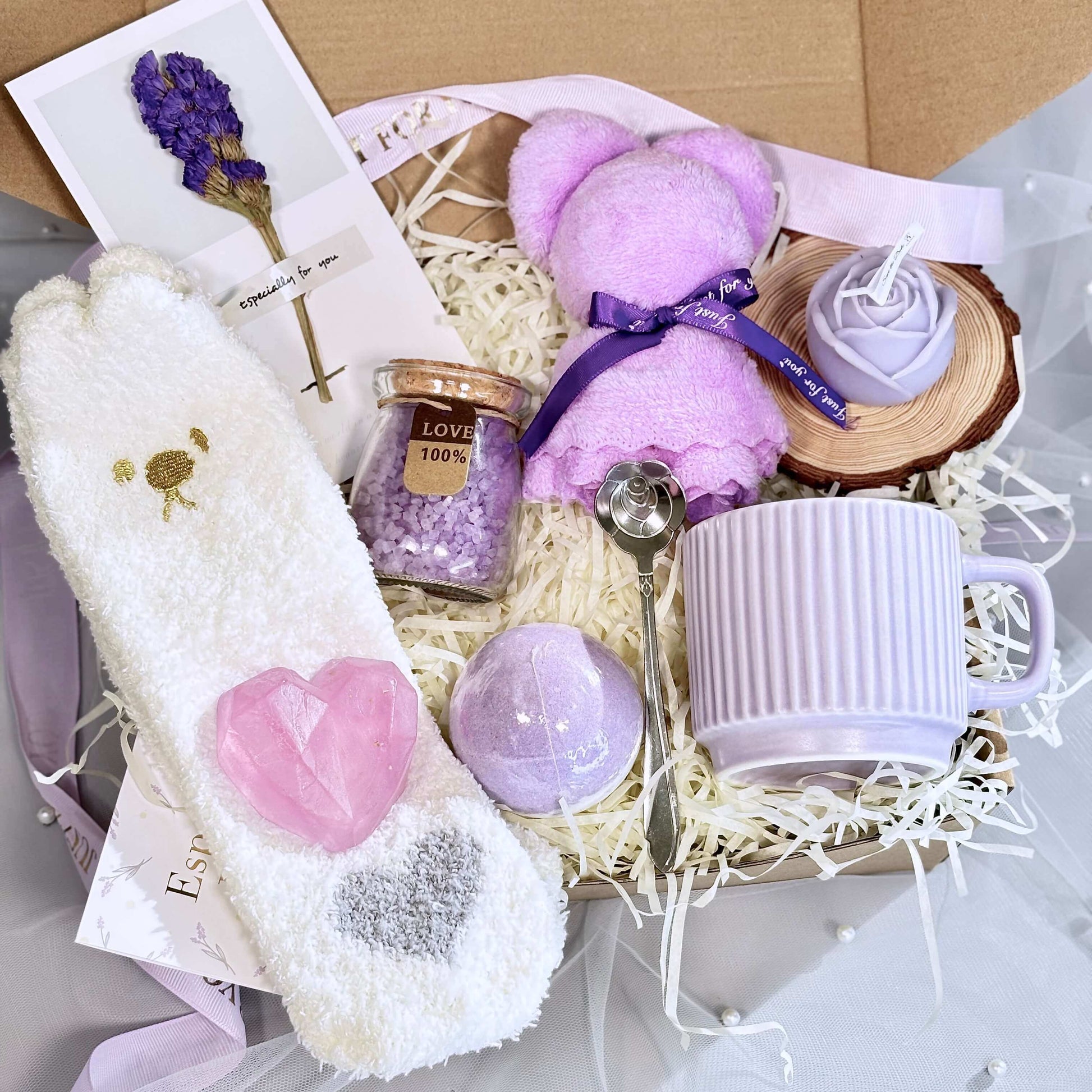 Lavender self-care gift box with mug, bath bomb, socks, pink heart soap, lavender salts, teddy candle, and greeting card inside packaging
