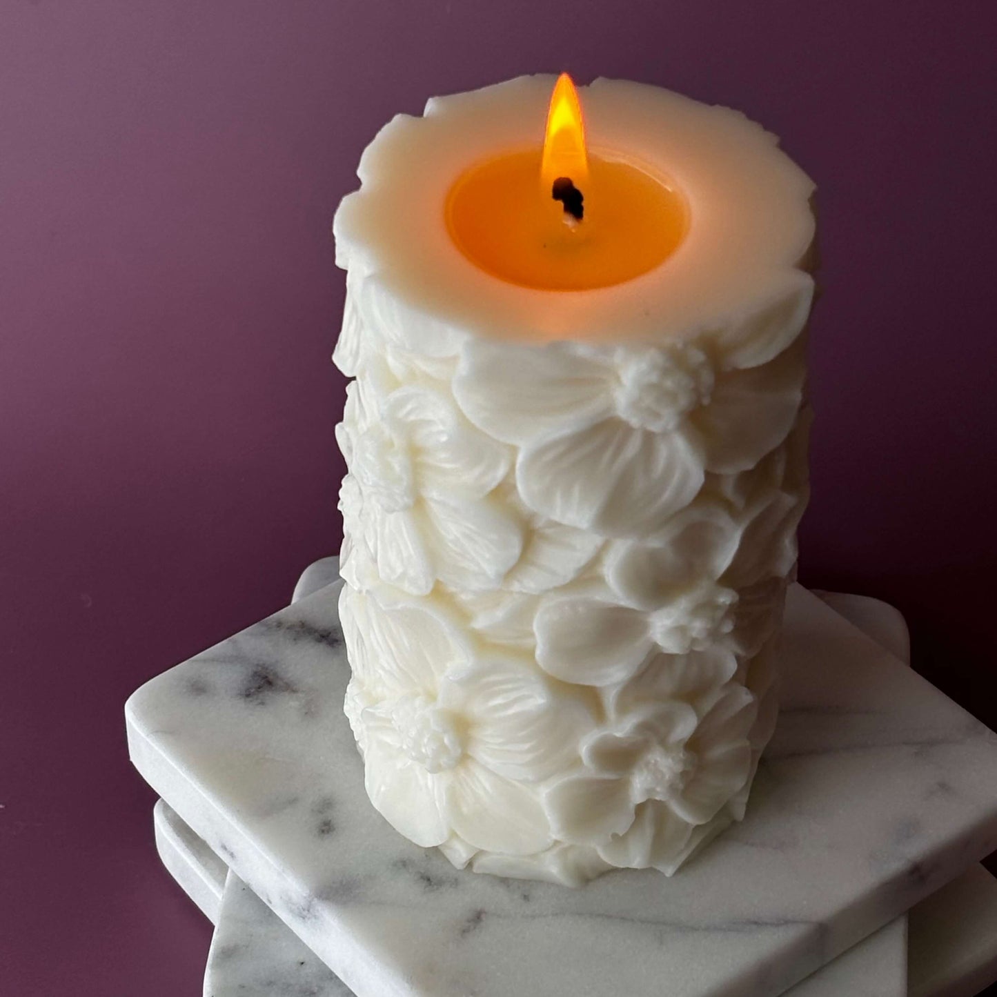 Burning Petal Lace soy pillar candle showing deep melt pool on marble coasters	