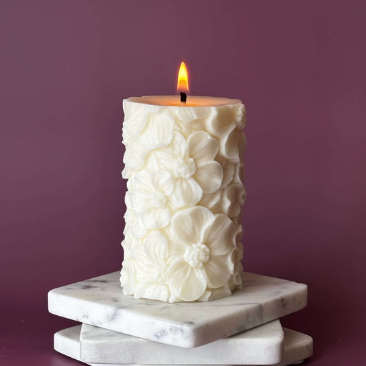 Lit floral soy pillar candle on stacked white marble coasters – handmade Petal Lace design	