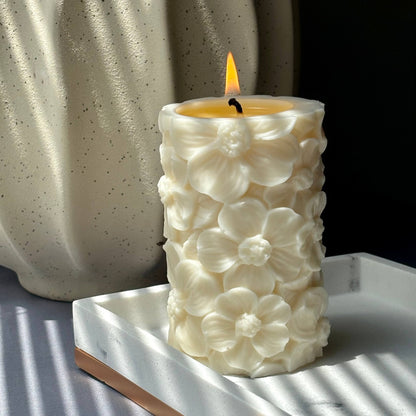 Lit floral soy pillar candle in natural light beside textured ceramic vase	