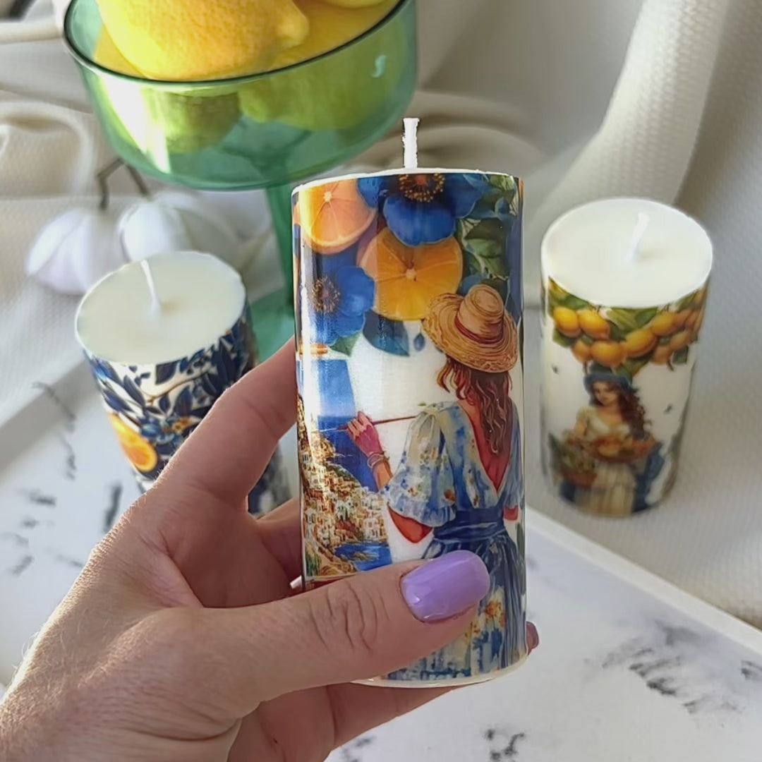 Three lit pillar candles with vibrant Italian-style prints featuring lemons, florals, and vintage portraits.