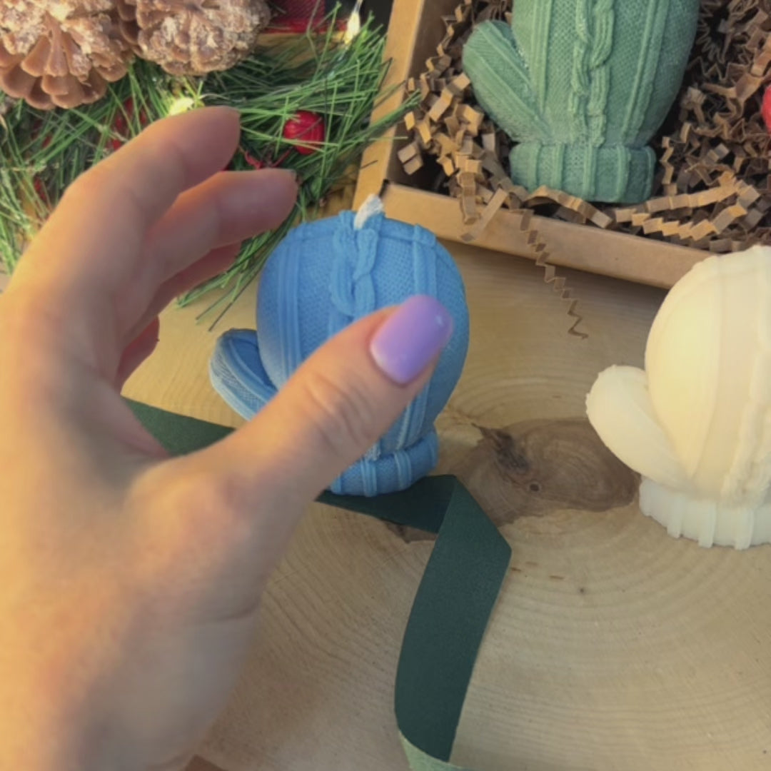 Hand touching blue mitten candle in cozy Christmas setup with soy wax gift set for winter decor