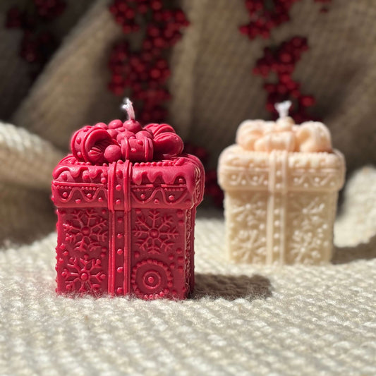 Red Christmas gift box candle with snowflake design, beige candle in background.