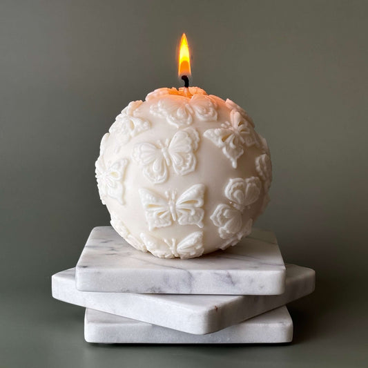 Round soy candle with butterflies, lit on marble tray
