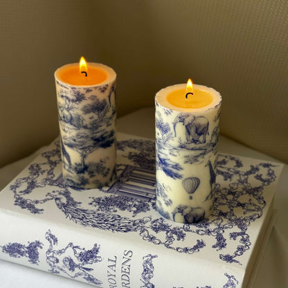 Two lit glossy candles with Toile de Jouy safari print placed on Royal Gardens decor book, perfect for elegant Afro-style table setting.