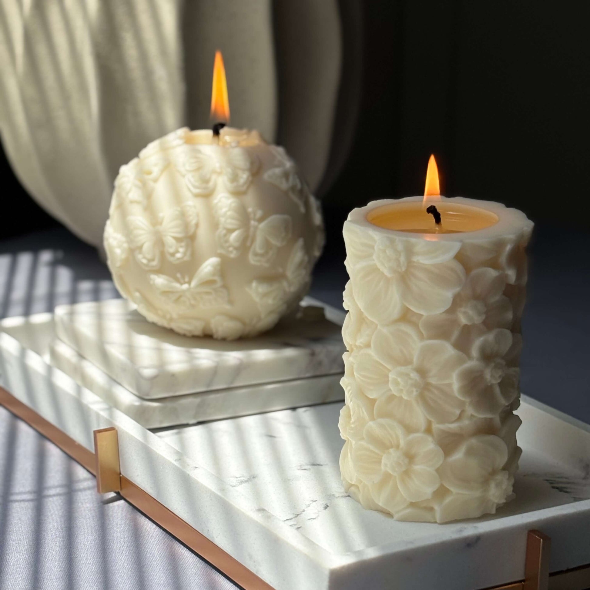Pair of sculpted soy candles – floral pillar and butterfly sphere burning on tray	