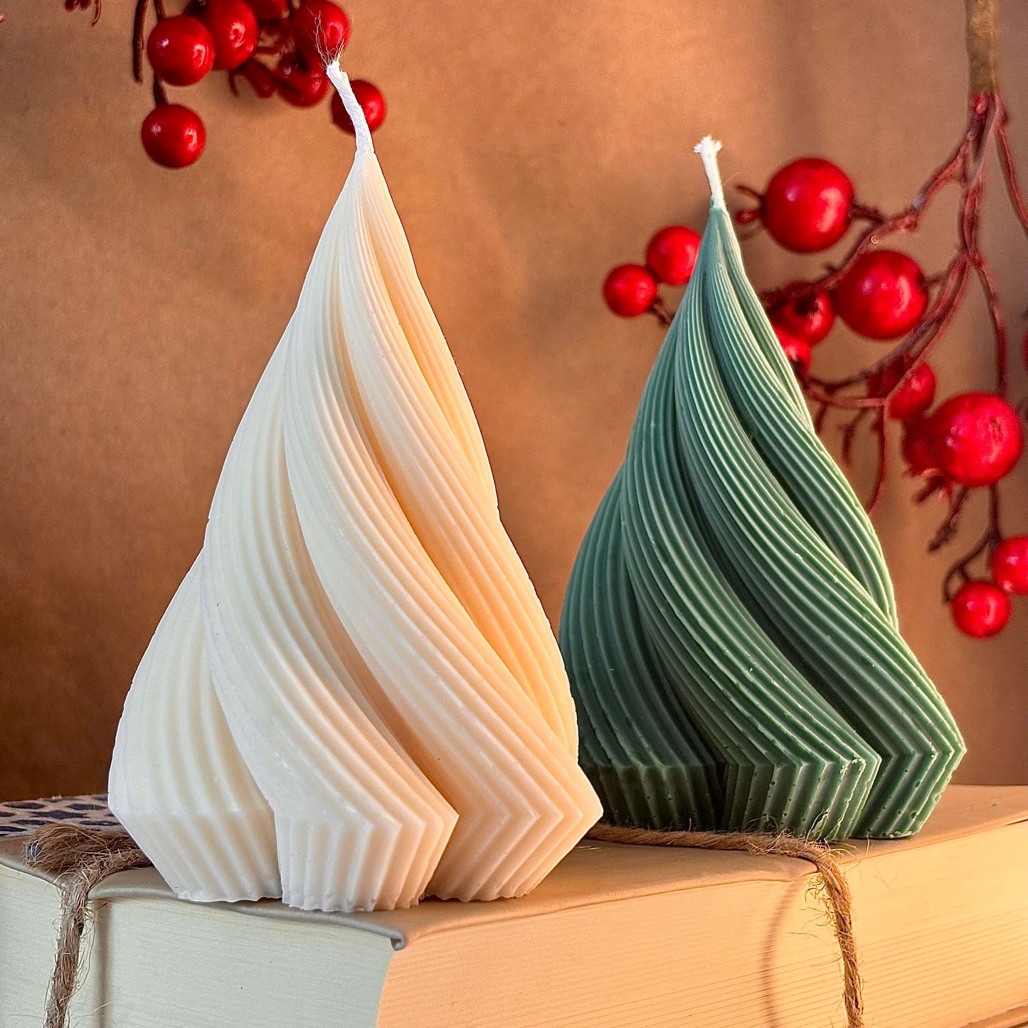 Close-up of ribbed sculptural candles in green and ivory, handmade soy wax, surrounded by red berry branches — Christmas gift decor

