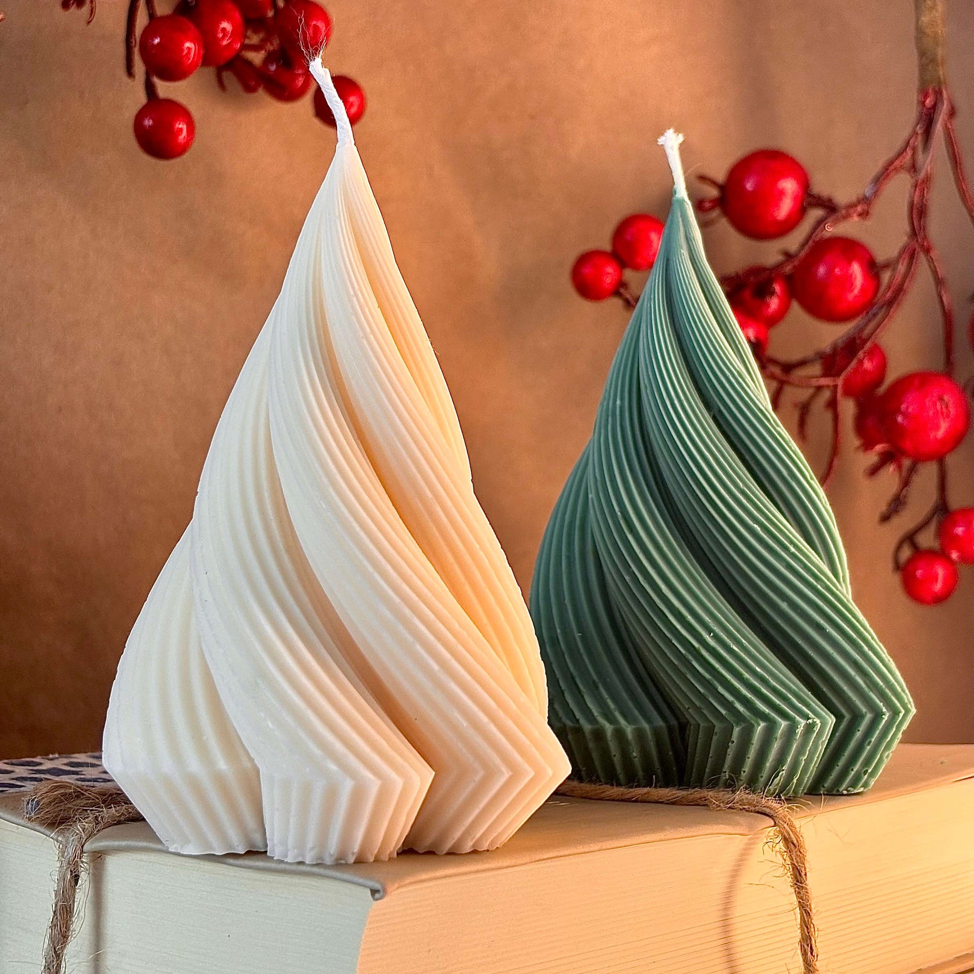Close-up of ribbed sculptural candles in green and ivory, handmade soy wax, surrounded by red berry branches — Christmas gift decor

