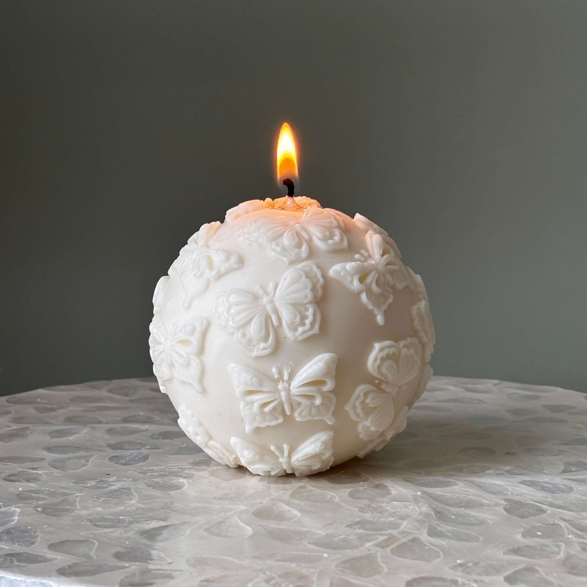 Lit soy wax candle with butterfly relief pattern
