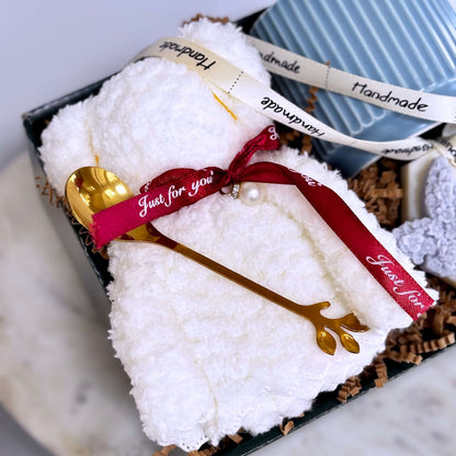 Close-up of fluffy teddy towel with red ribbon and gold branch-style spoon inside luxury gift box — cozy self-care gift idea for her, birthdays, or appreciation moments