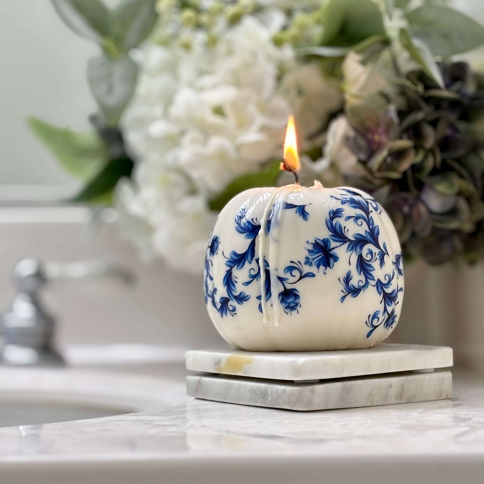 Holiday-ready pumpkin candle with glossy white finish and blue floral print, styled as a luxury seasonal gift in a cozy bathroom setting.