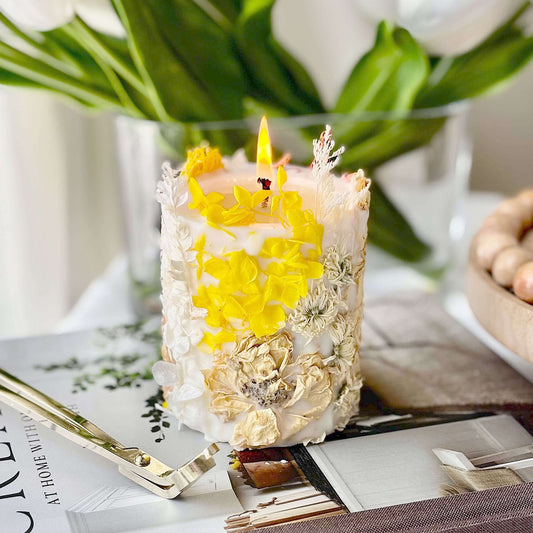 Handmade botanical soy candle with pressed yellow flowers, burning on a table. Elegant home decor made in California.